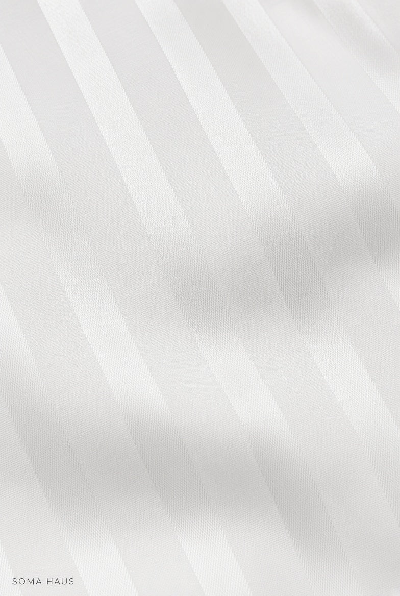 A close-up of a white or off-white striped fabric with soft diagonal bands and a subtle woven texture. Small text in the lower-left corner reads SOMA HAUS.