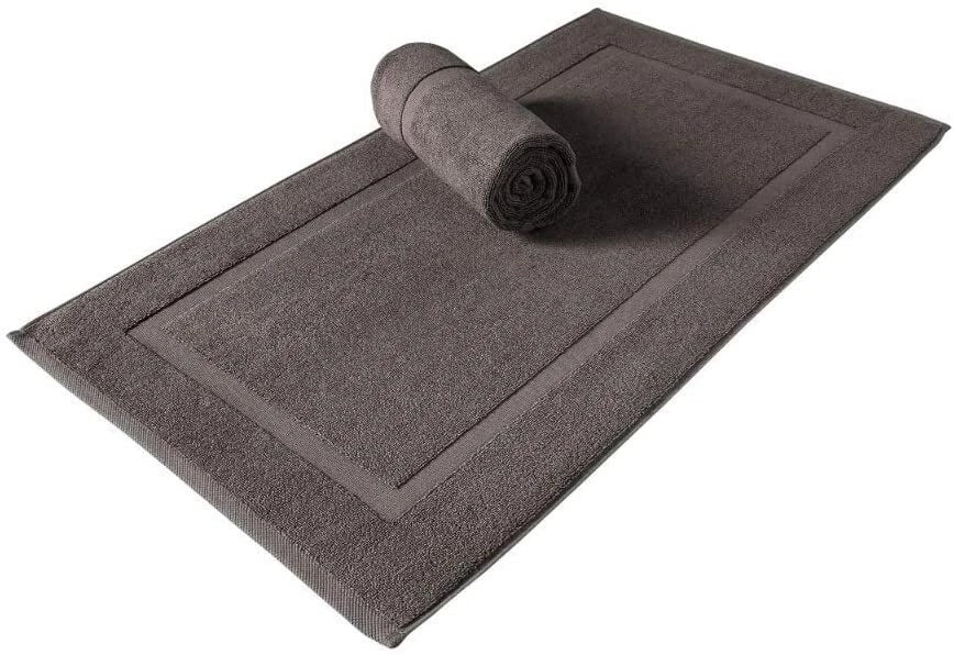 A dark brown rectangular bath mat with a raised border, shown on a white background with a matching rolled towel placed on top.
